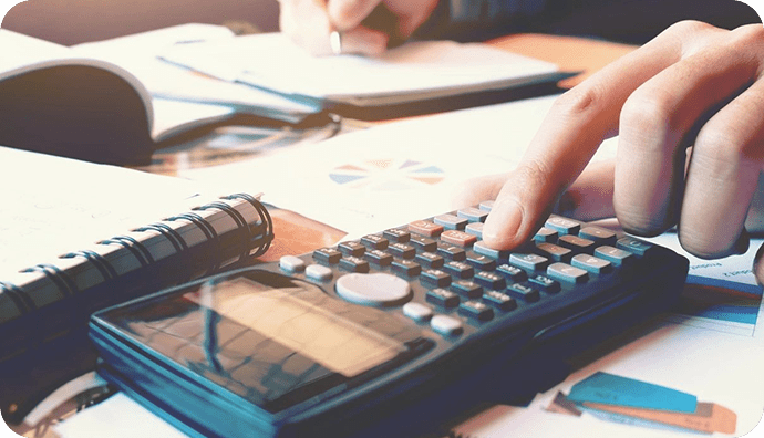 Person using a calculator with notebooks and papers on a desk, suggesting a focus on finances or academic work.